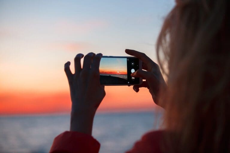 A woman captures the breathtaking sunset with her cell phone, creating stunning photographs during her Turkish adventure.