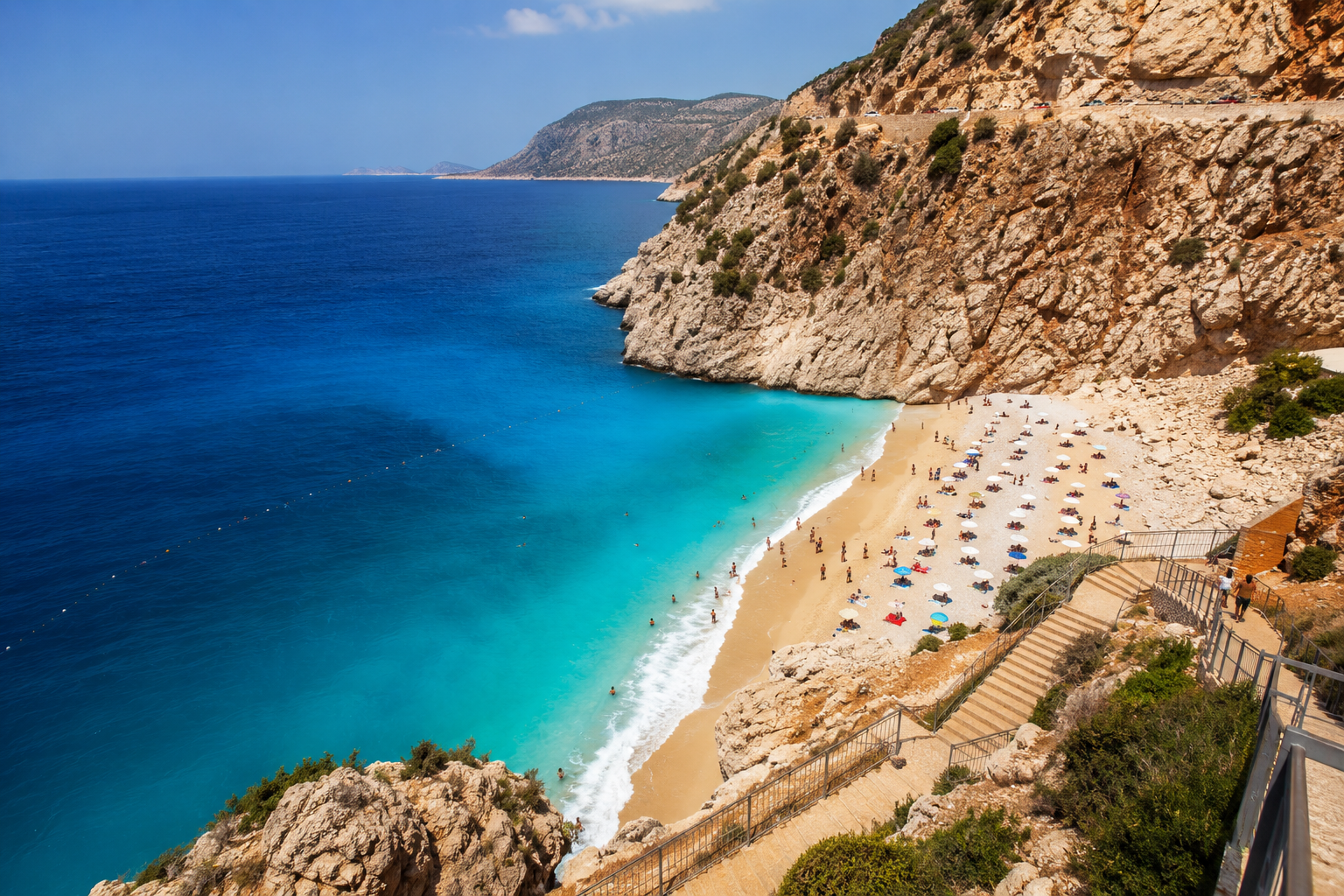 () dramatic wide-angle photograph of Kaputaş Beach viewed from the famous D400 highway staircase above, showing the tiny
